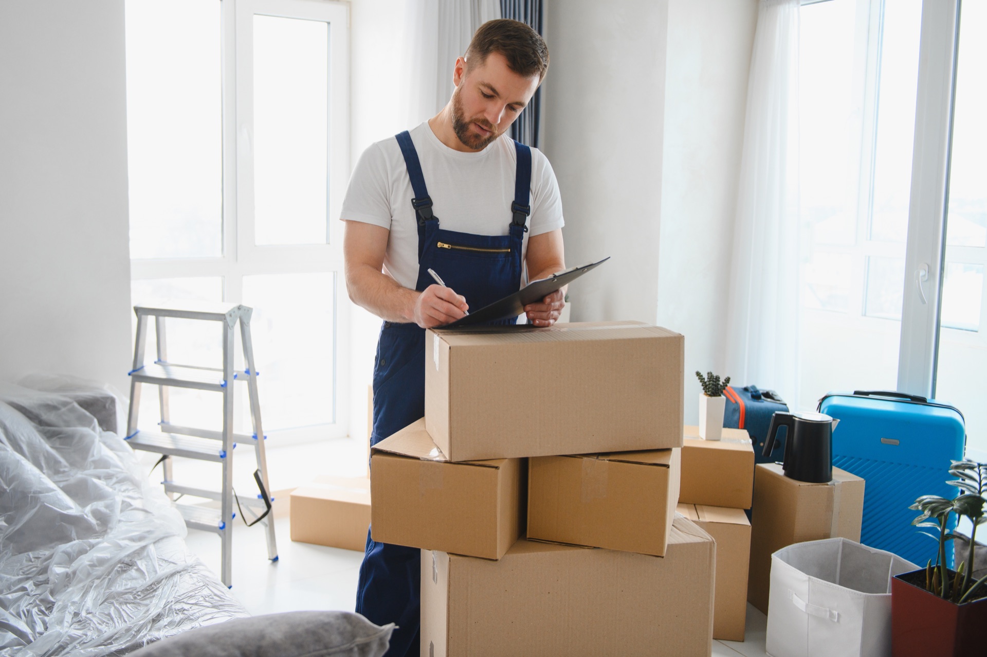 Mover taking inventory beside stacked moving boxes in a home